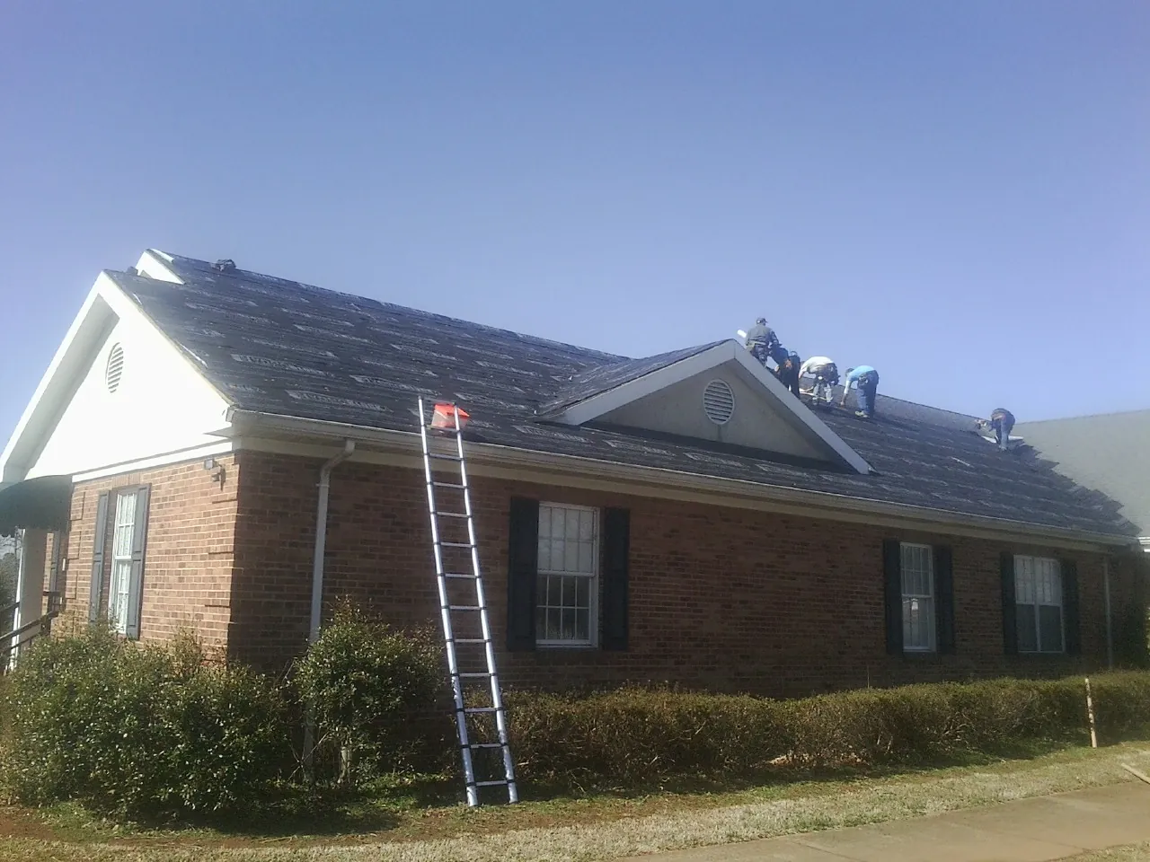 Crew tearing shingles off a brick ranch roof with a ladder set — Metal Roof Repair work by our crew in Tiffin