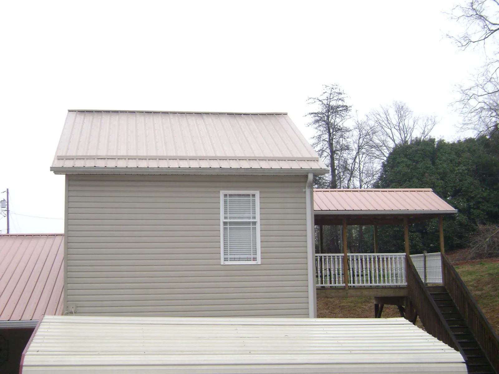 Tan metal roofs on a two story addition and attached porch, from a Roof Replacement job in Tiffin